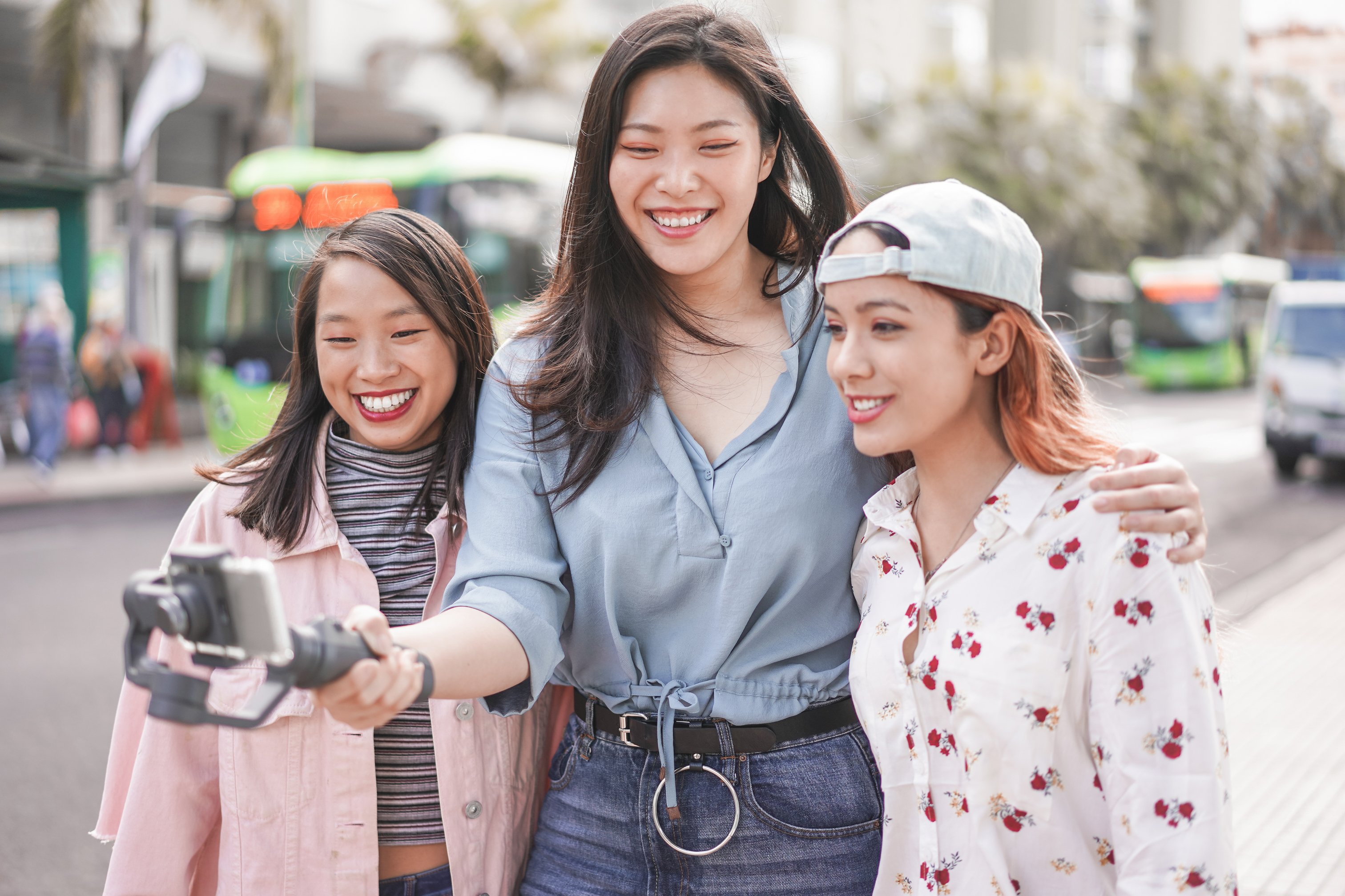 Three young women stream a live video outside.