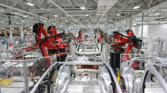 Car assembly line, with frames of vehicles and red robotic arms.