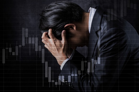 A roller coaster stock chart superimposed over a man with his head in his hands.