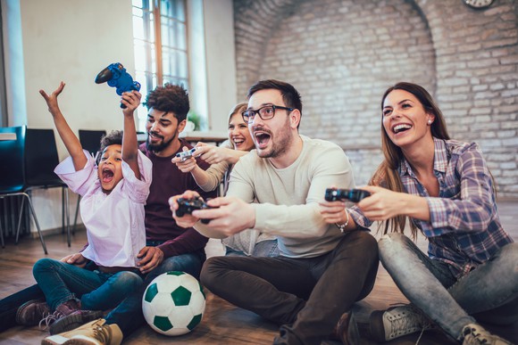 A group of men and women and a young girl sitting on the floor playing video games.