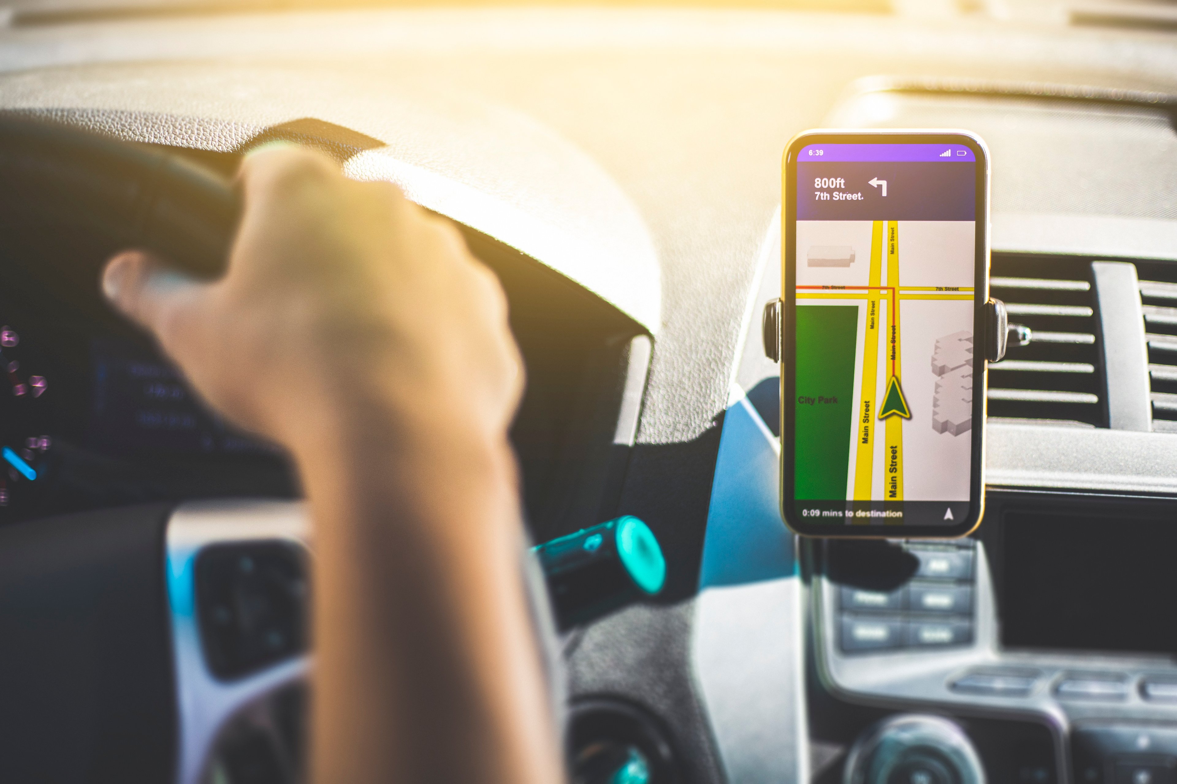 A person driving a car. A smart-device displaying directions is on the dash.