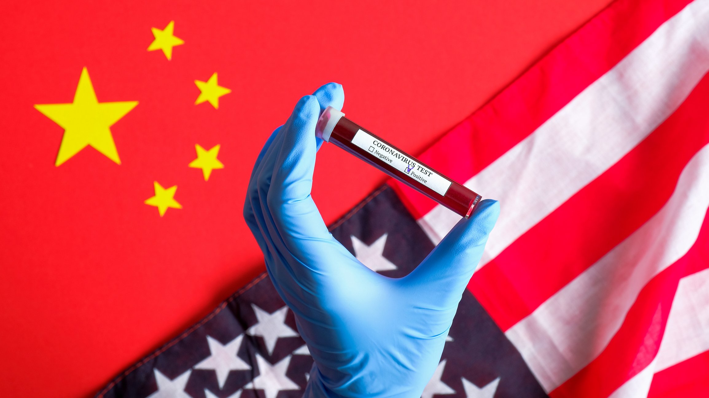 A person holding a COVID-19 test in front of a Chinese and an American flag.