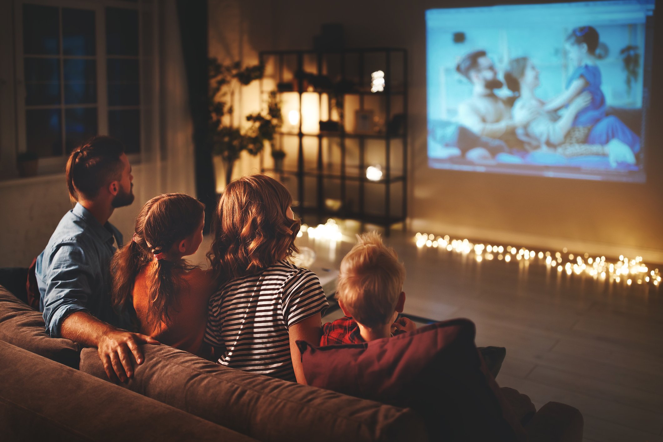 A family of four sitting on a couch together watching a movie.