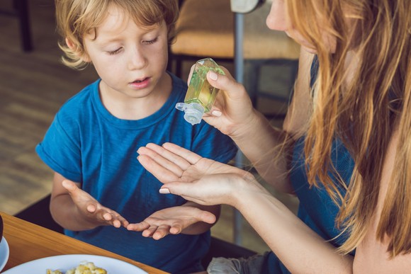 Mother applying hand sanitizer to her hands and her son's