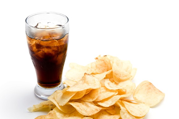 Glass filled with ice and cola next to some potato chips