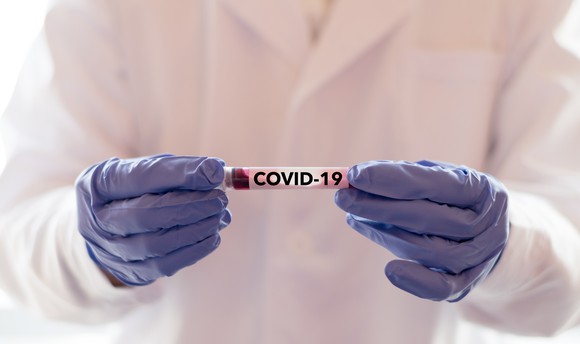 Closeup on gloved hands of  clinician holding a test tube with the label COVID-19. 