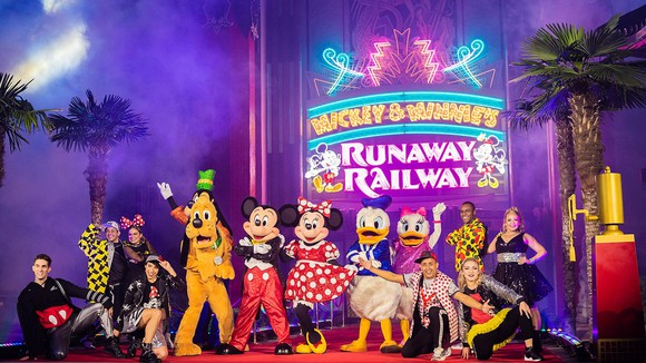 Mickey Mouse and several costumed characters and Disney performers in front of the Mickey & Minnie's Runaway Railyway marquee.