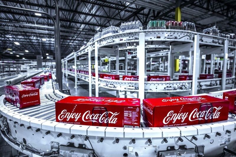 cases of Coca-Cola cans roll along an assembly line conveyor in a bottling plant