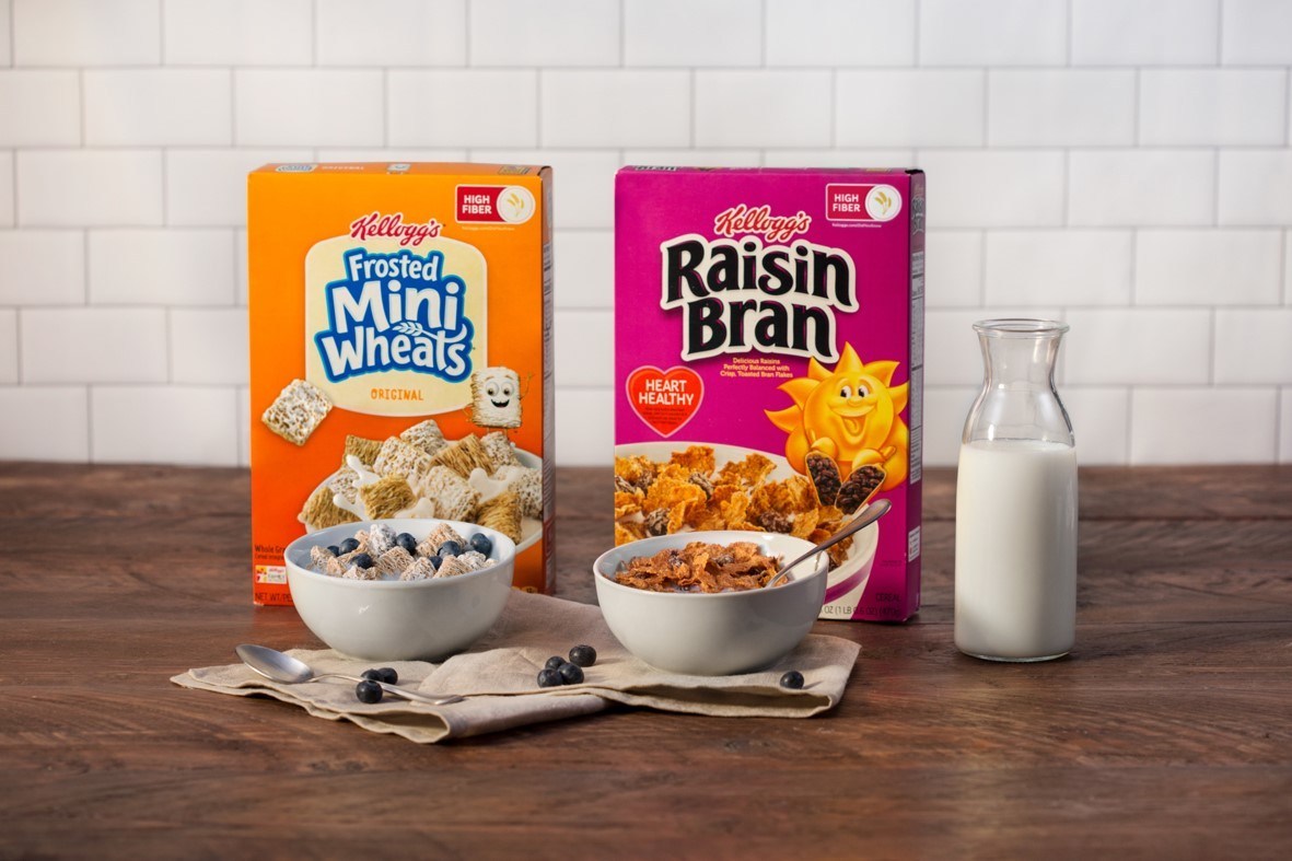 Kellogg cereals Mini Wheats and Raisin Bran sit on a table with bowls and a glass pitcher of milk