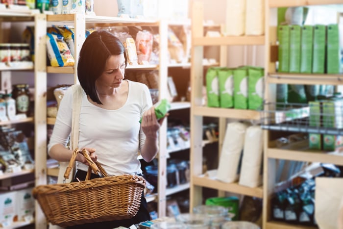A woman at a store holding a basket while looking at an item.