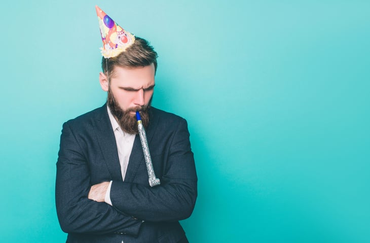 A businessman in a party hat with a disappointed look on his face.