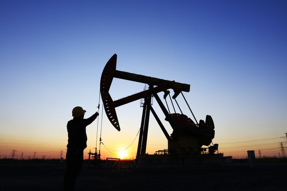 The silhouettes of workers and machinery in an oilfield at dawn.