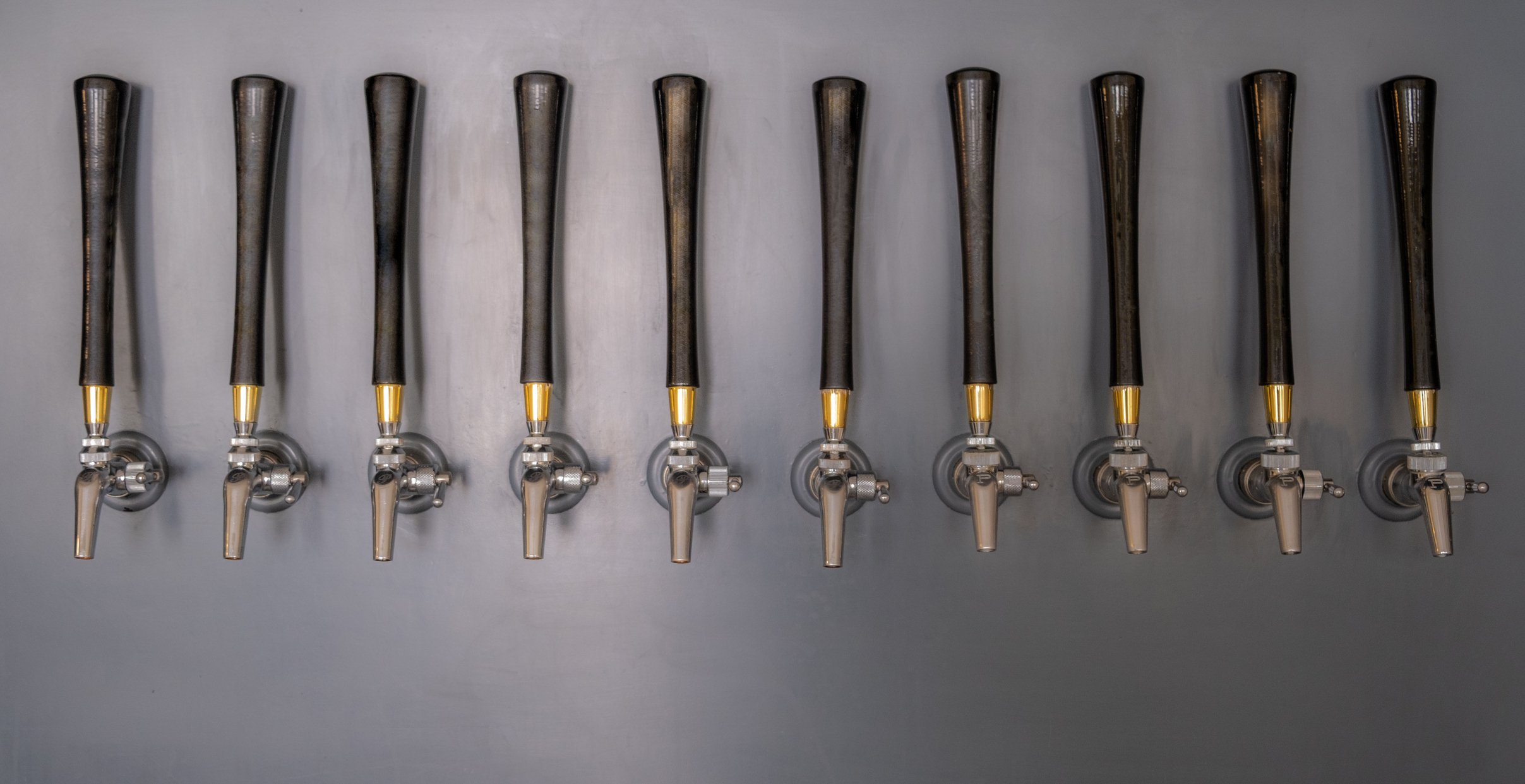 10 beer taps with long wood handles mounted on a grey slate wall.