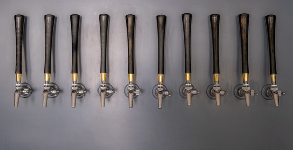 10 beer taps with long wood handles mounted on a grey slate wall.