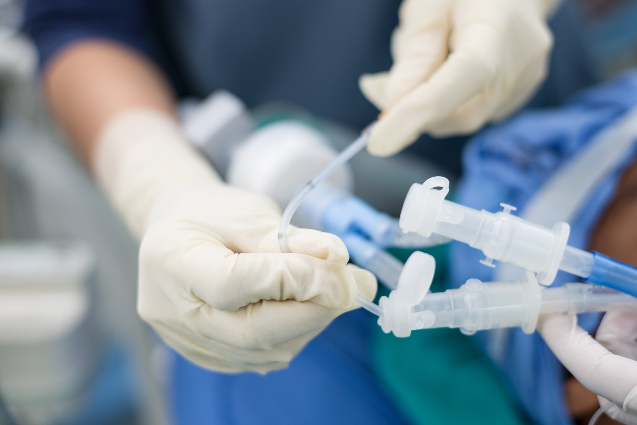 A pair of hands in surgical gloves inserts a tube into a respiratory device.