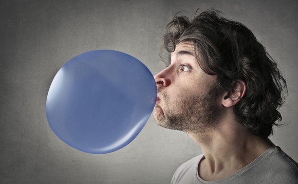 A young man blows a big purple balloon. 