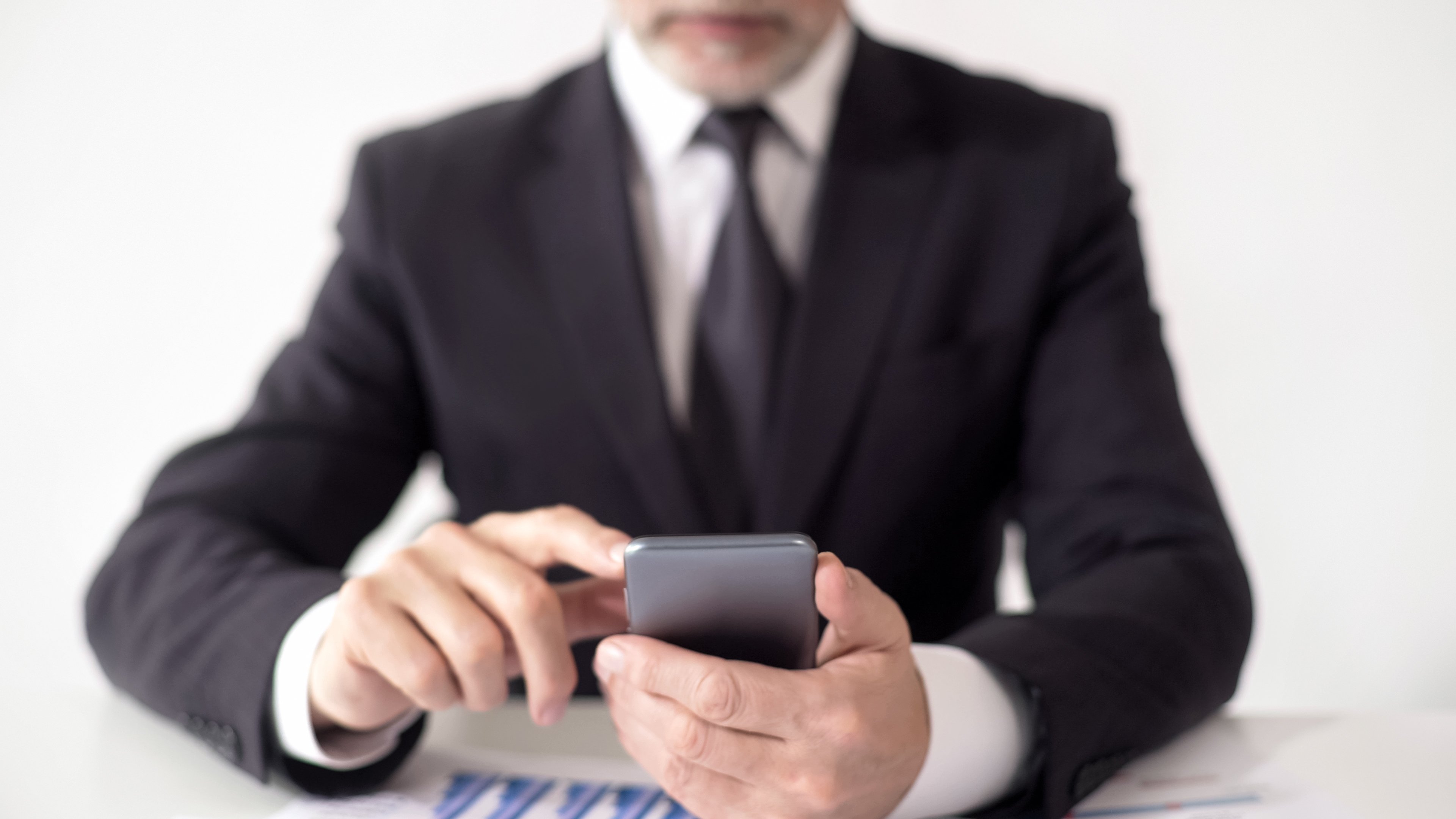 Businessman seen from neck down punches buttons on a handheld calculator at a desk. 