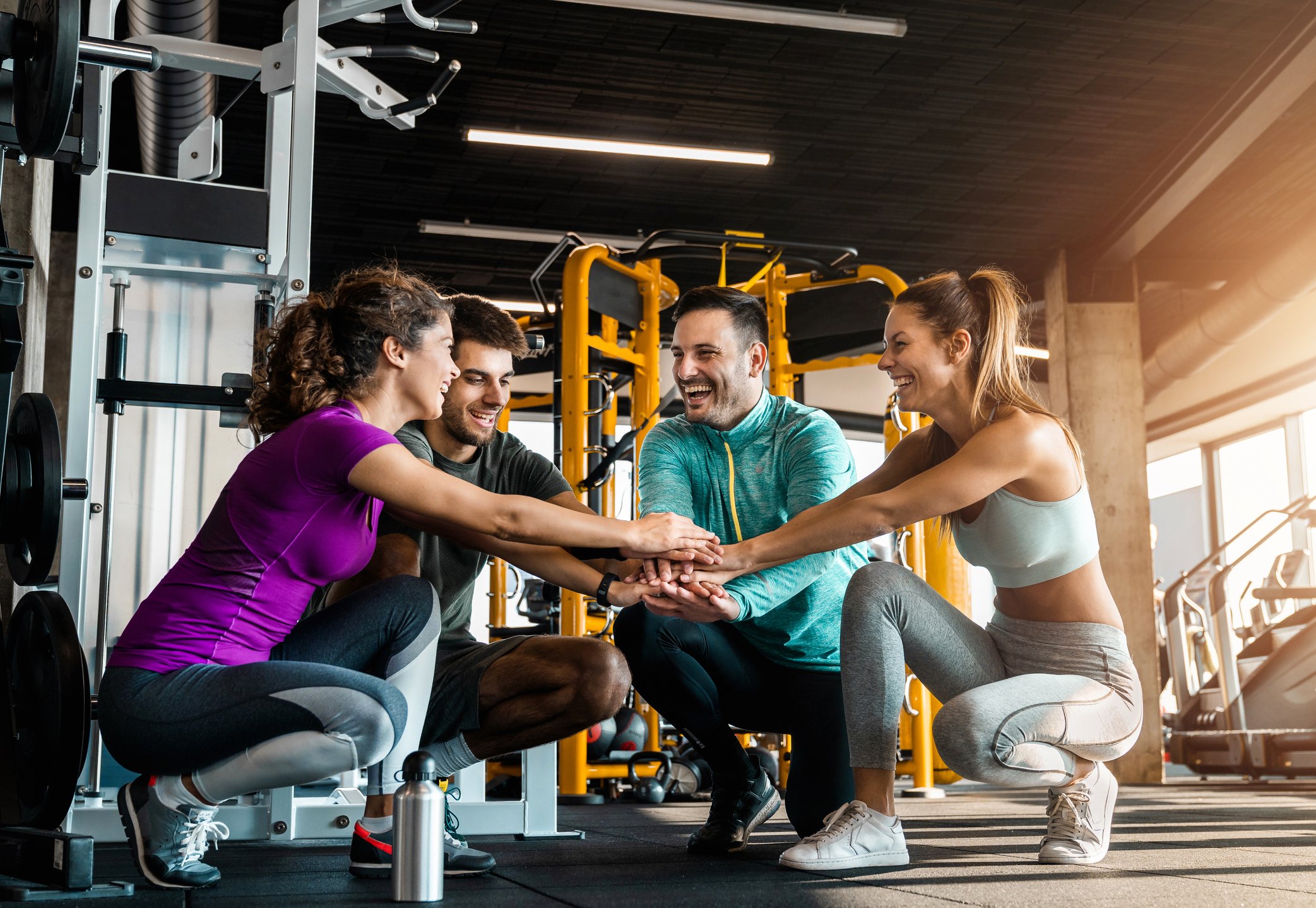 A group of men and women in a workout gym putting their hands together.