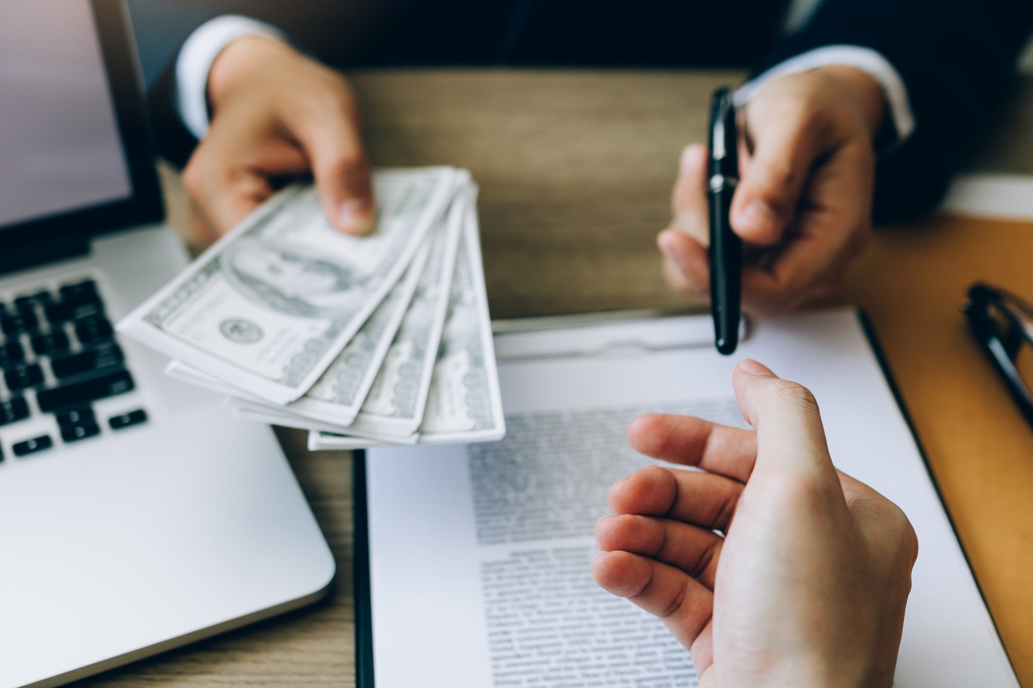 A banker holding money and a pen about to provide a customer with a loan.
