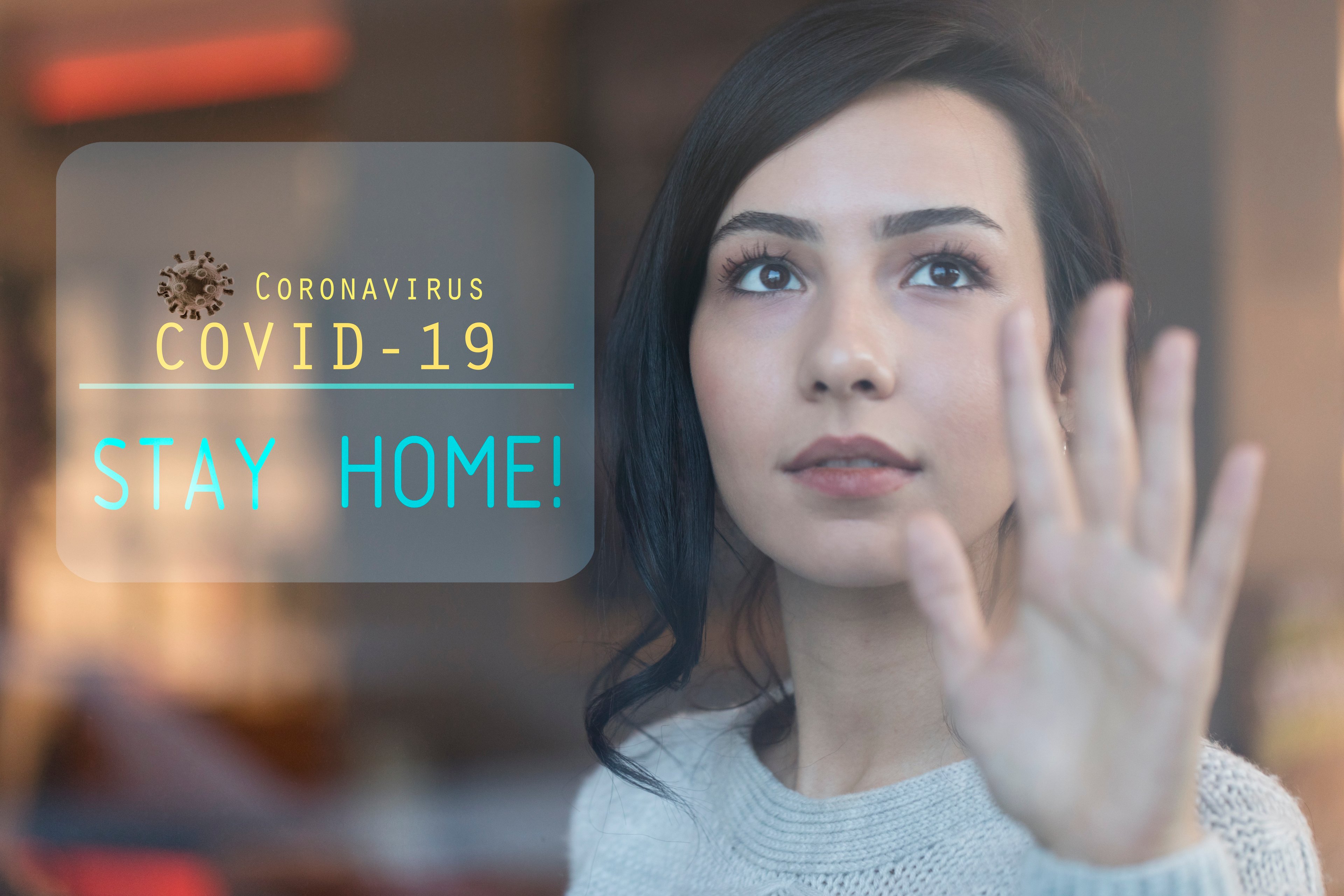 Woman looking out window with stay home sign. 