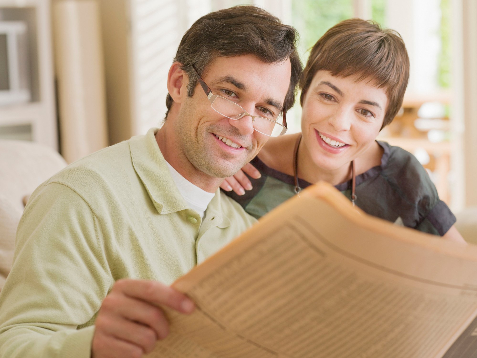 A smiling couple reading the financial section of a newspaper.