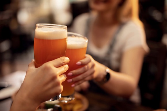Two women drink beer outside.