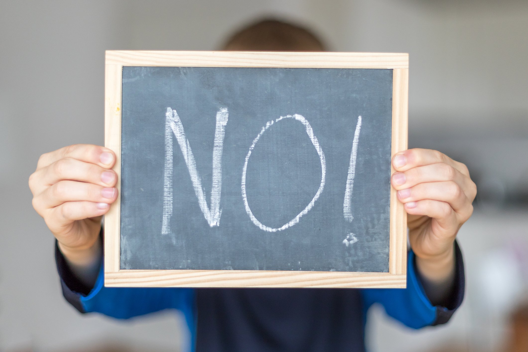 A man holds up a small chalkboard with the word no written on it in chalk. 