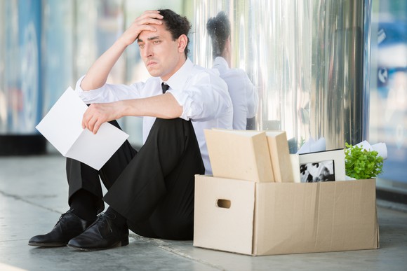 Man sitting next to big box of office supplies, holding his head with one hand and a document with another