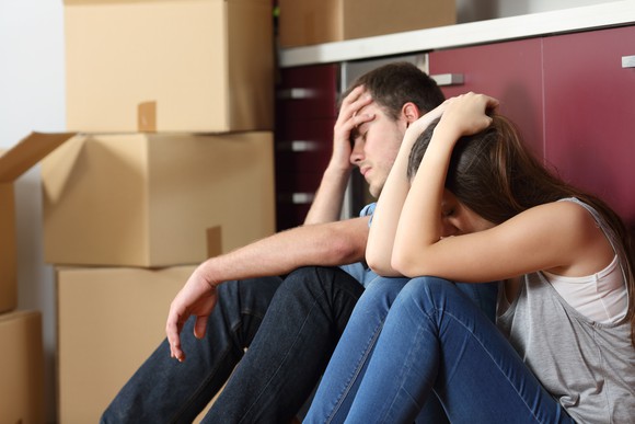 Couple with moving boxes sitting holding their heads