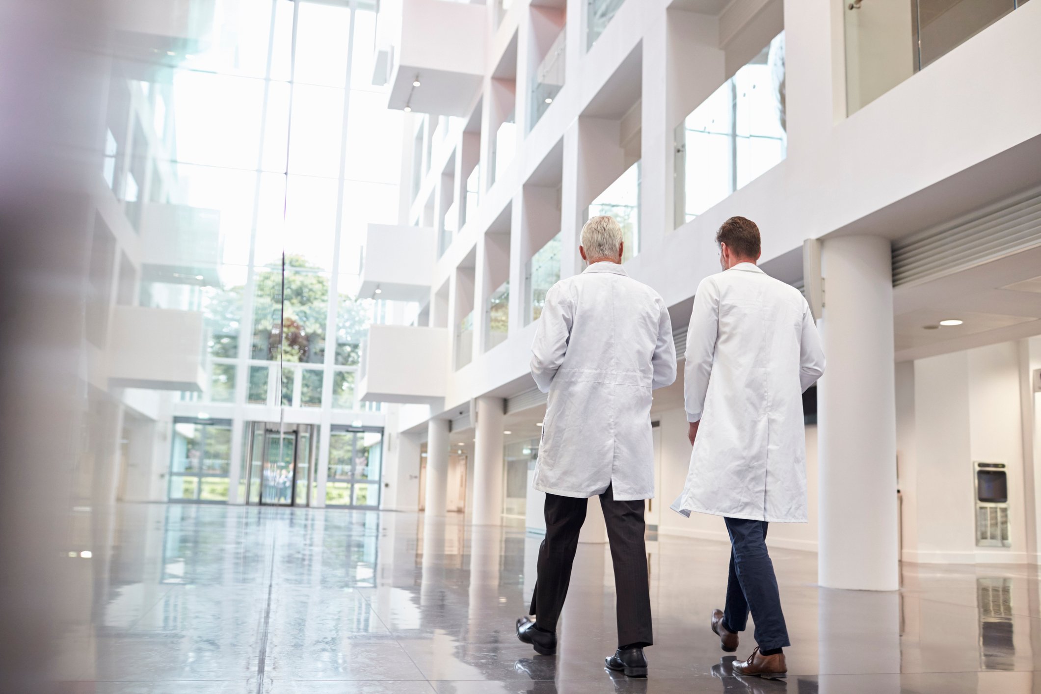 Two people wearing white lab coats in an atrium in a building.
