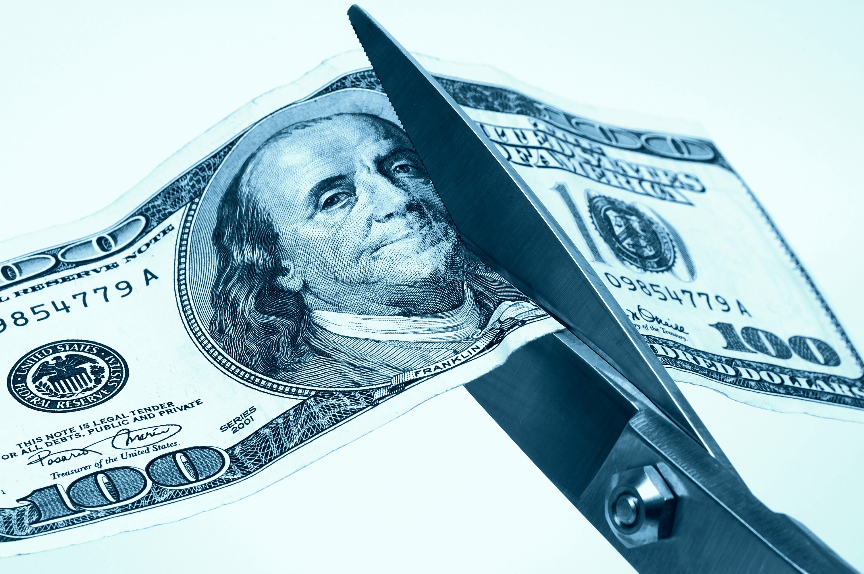 A hundred dollar bill being cut with scissors. 