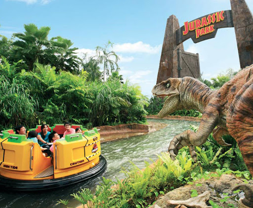 The Jurassic Park ride at Universal Studios. A raft on a river full of visitors with a dinosaur pictured in the foreground.