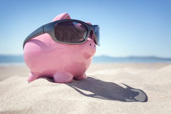 A pink piggybank with black sunglasses sits on a beach.