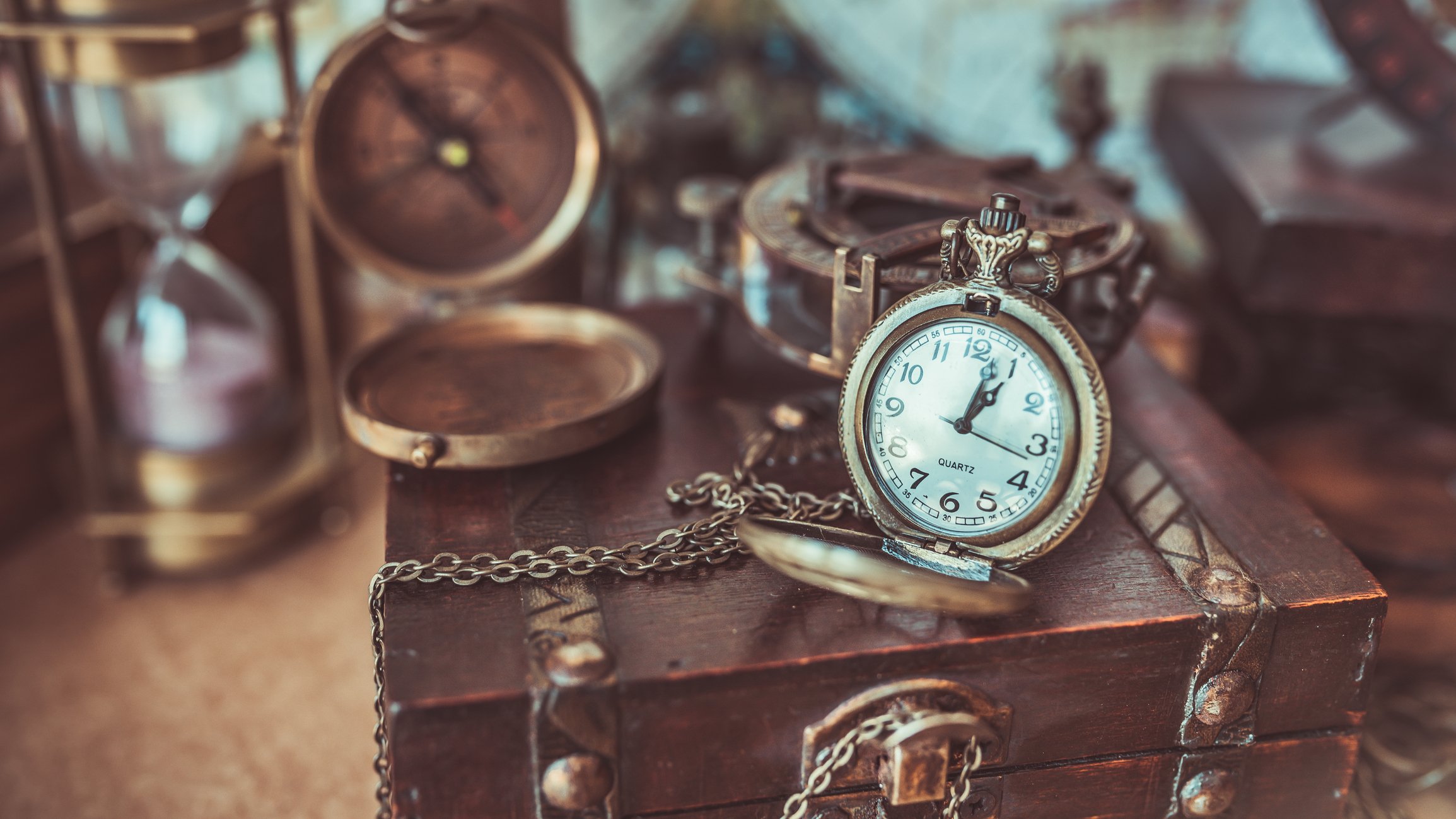 Numerous antiques including a compass, a pocket watch, and an hourglass arranged on a table.