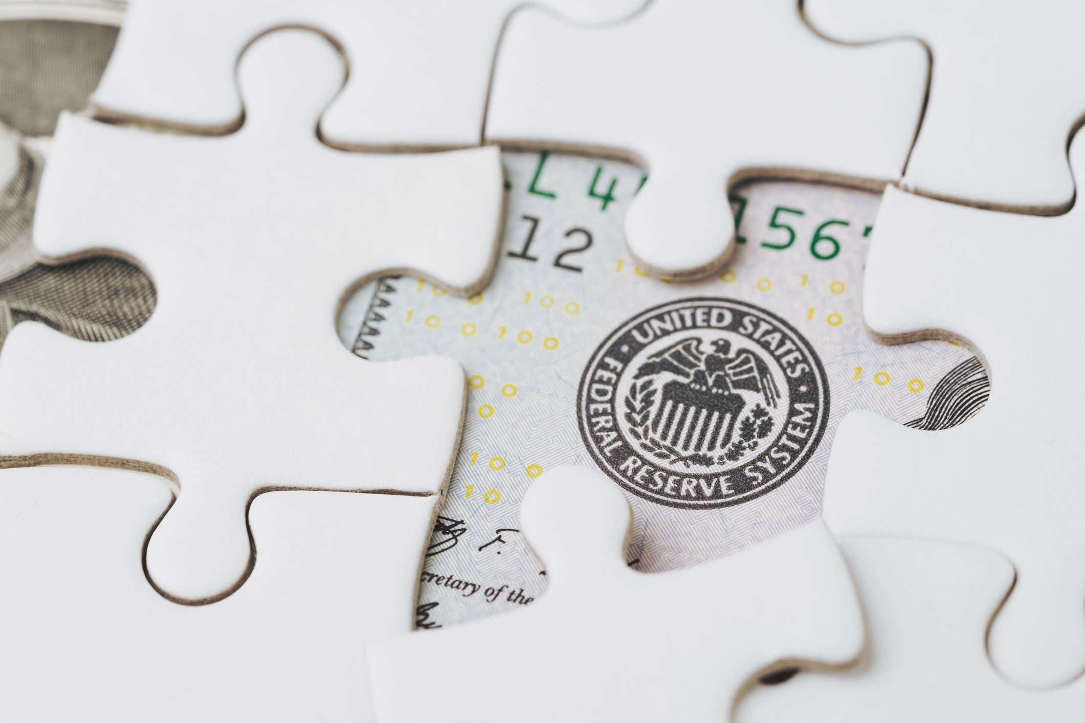 A jigsaw puzzle over a U.S. bill revealing the seal of the Federal Reserve