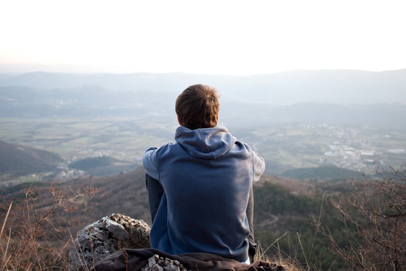A young man sitting on a mountainside and staring into the horizon.
