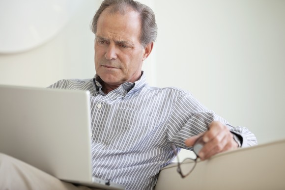 Older man with a serious expression on his face, looking at his laptop.