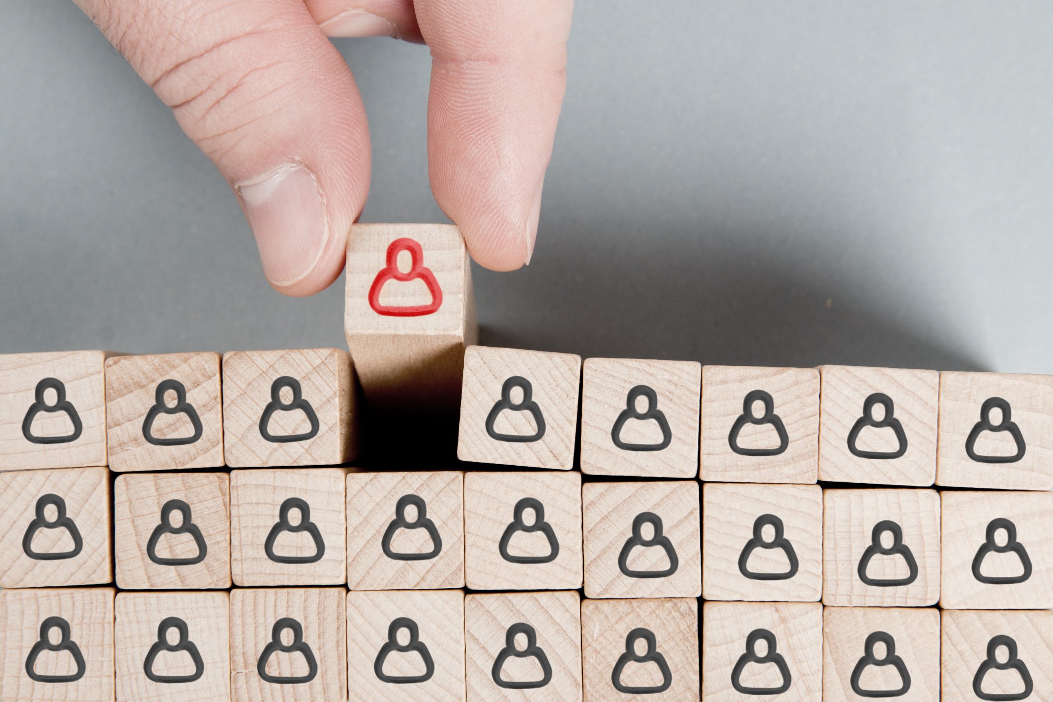 A hand selecting one misfit from a uniform group of wooden blocks