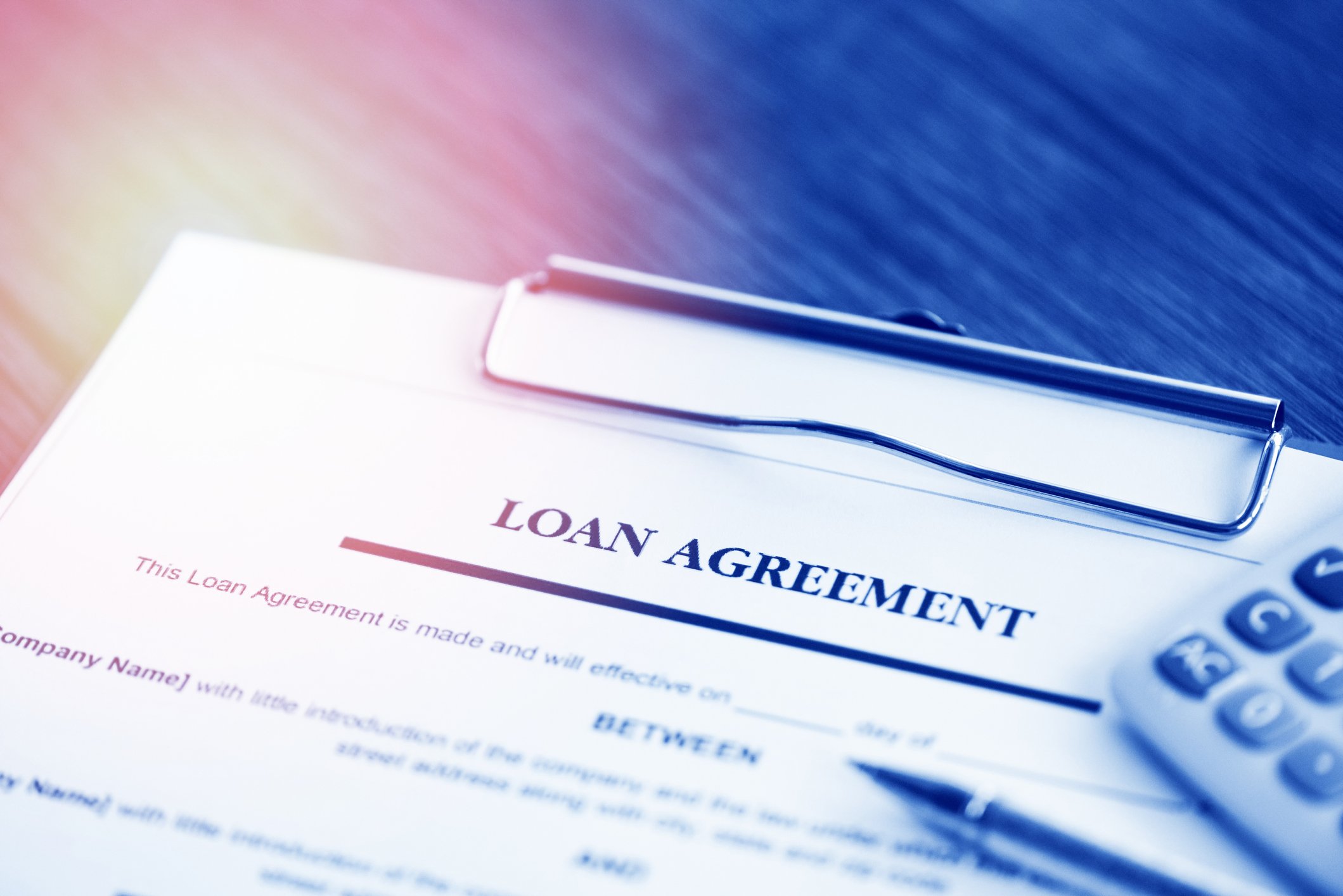 A document that says "loan agreement" with a calculator and pen laying on top of it. 