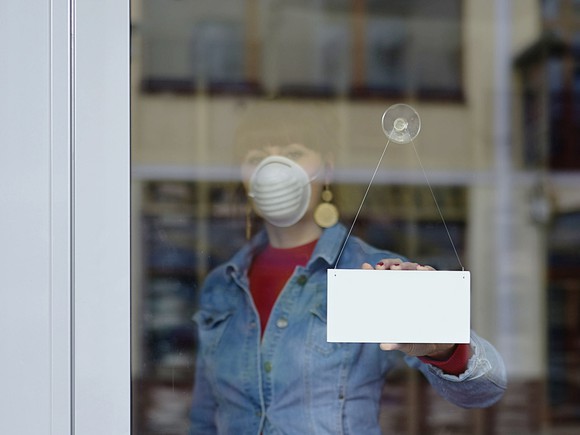 Woman in mask turns store window sign around.