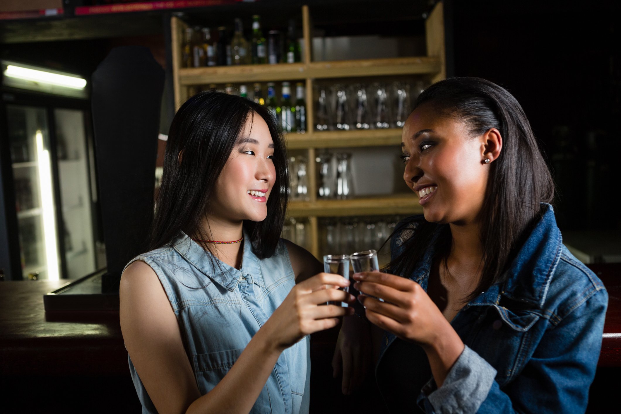 Two women in a bar about to drink shots of premium alcohol.