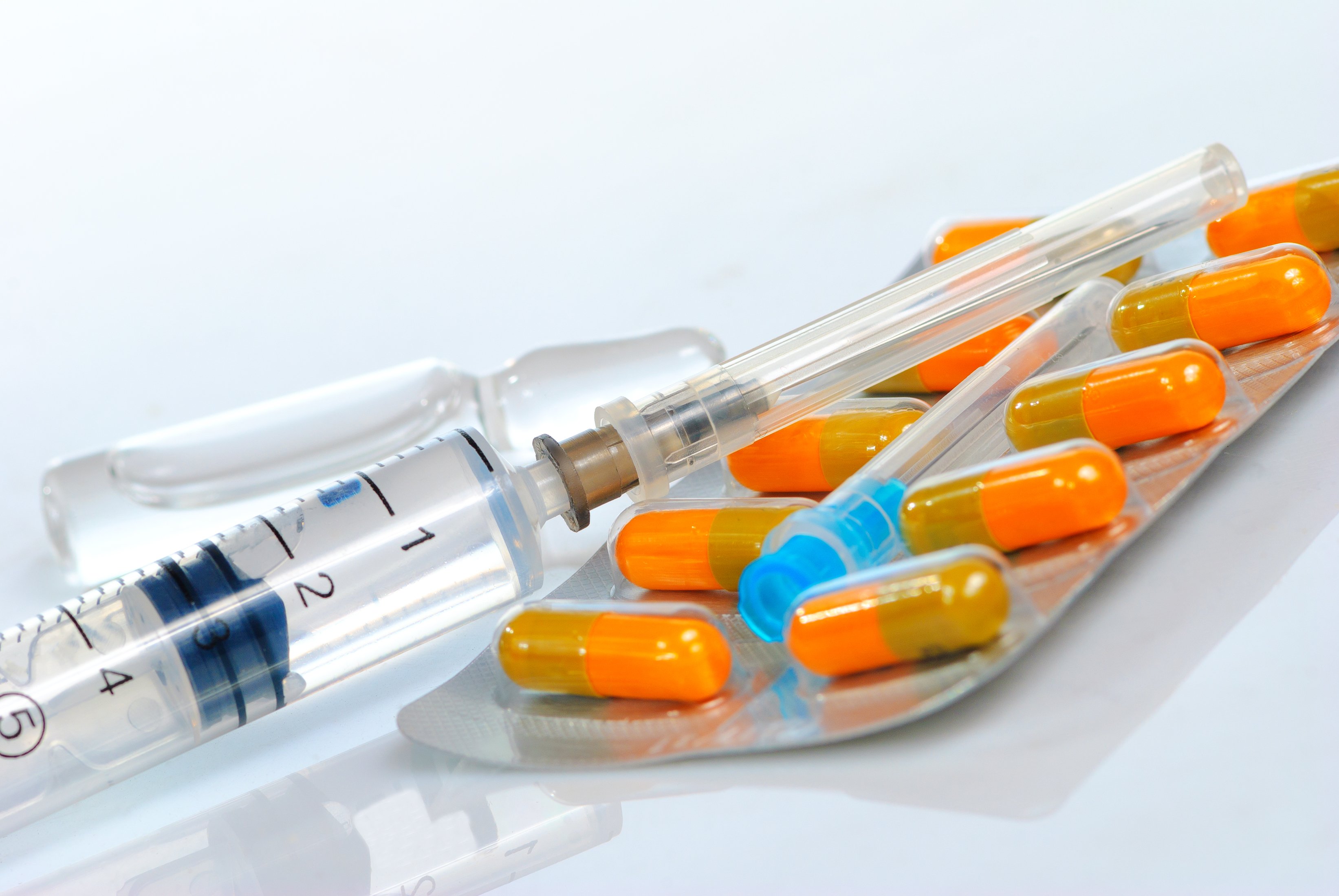 Syringe next to blister pack of orange and brown capsules