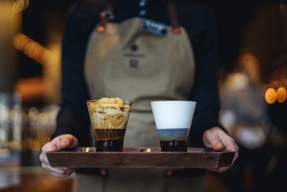 Starbucks worker holding two drinks on a tray.