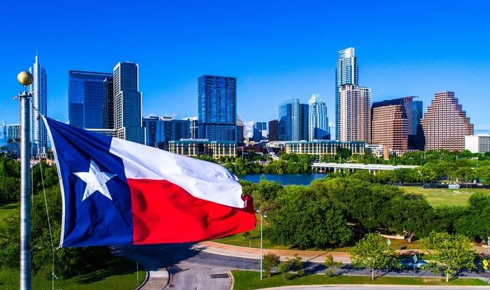 Texas flag flying in front of Austin skyline.