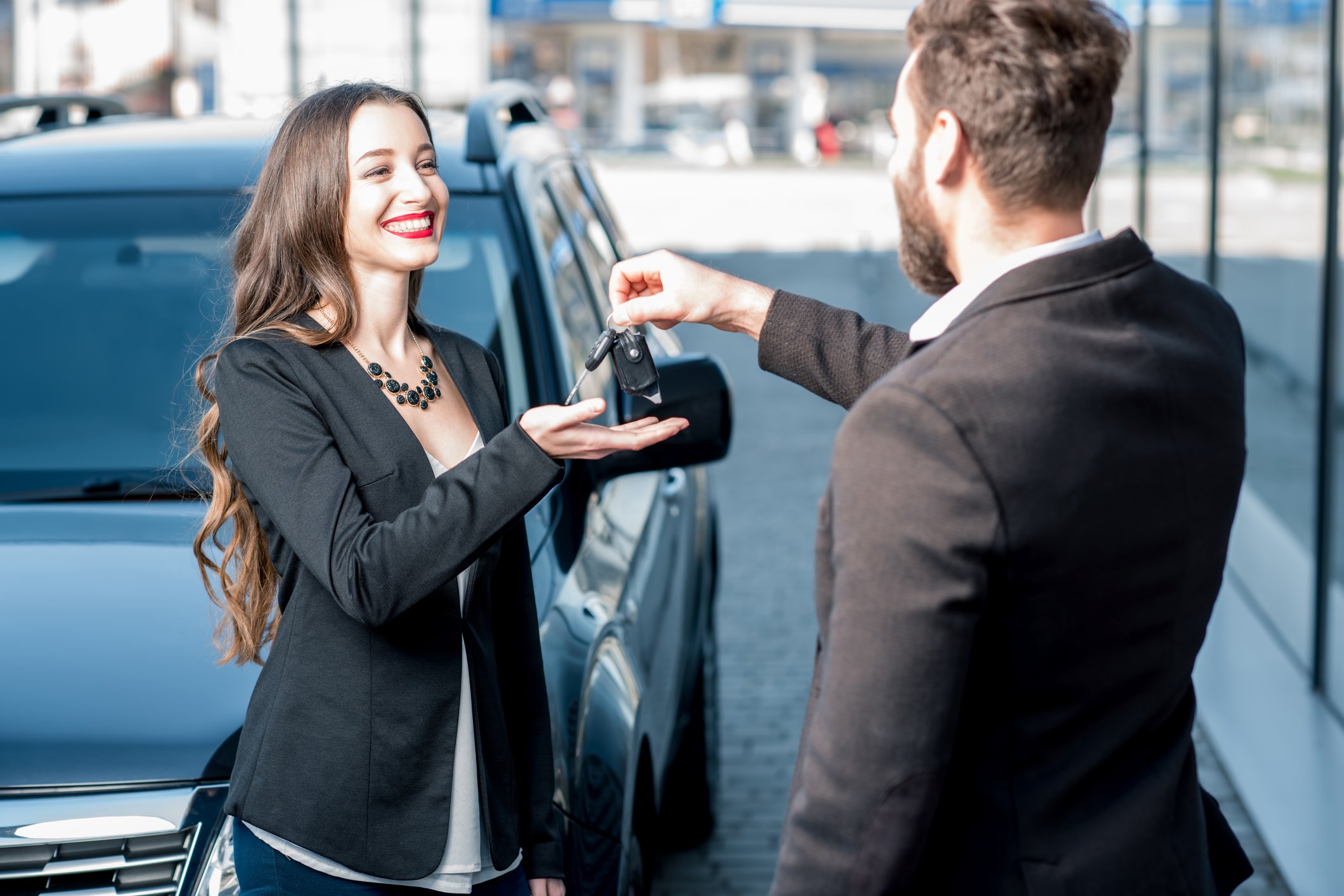 A used car salesman hands keys to a smiling customer.