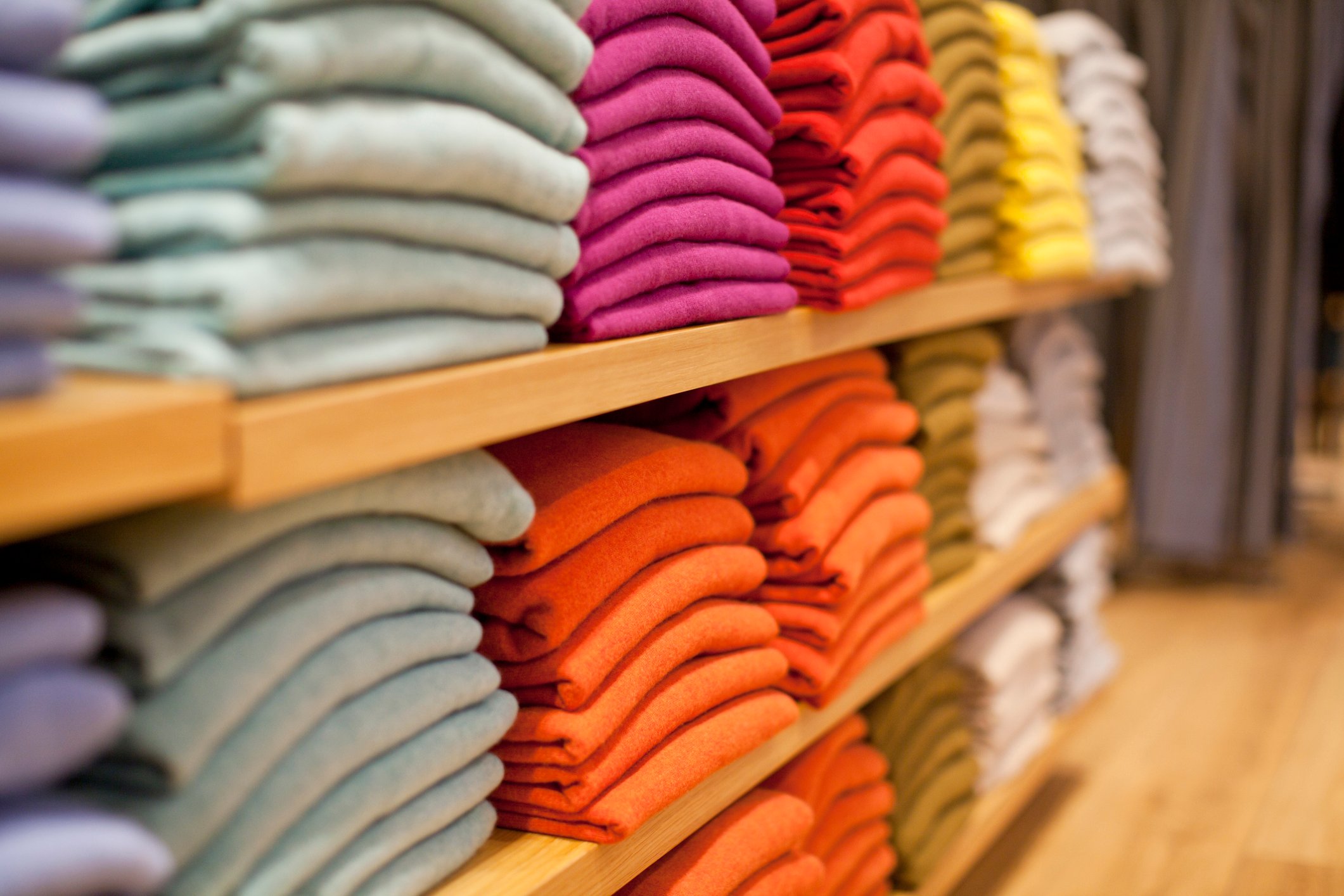 Sweaters in gray, pink, orange and other colors are stacked on store shelves.