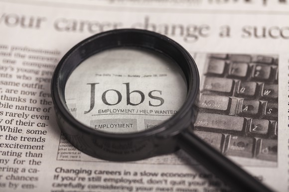 Resting on a newspaper, a magnifying glass focuses on the word jobs.
