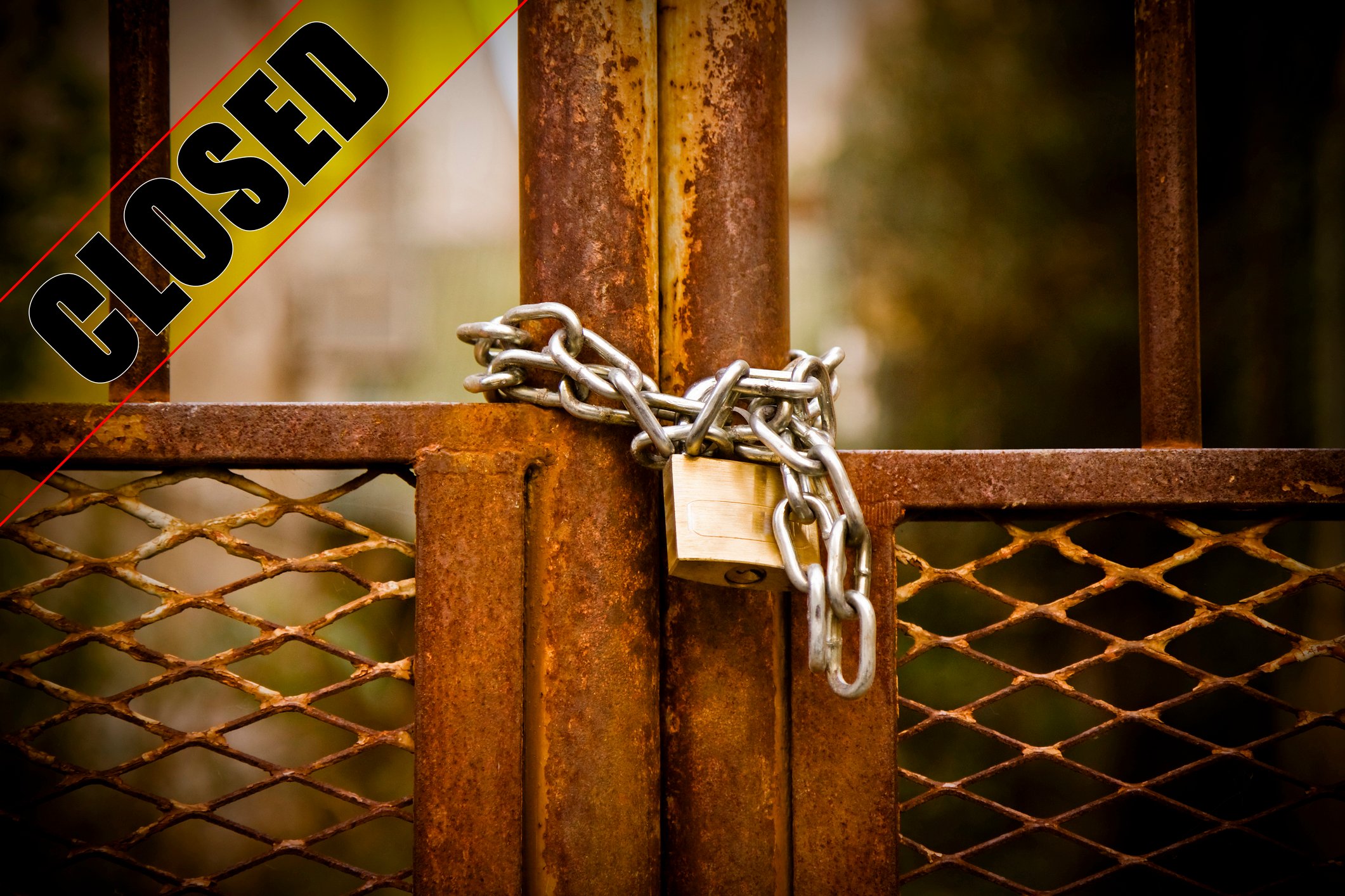 A lock and closed sign on a factory metal gate.