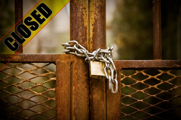 A lock and closed sign on a factory metal gate.