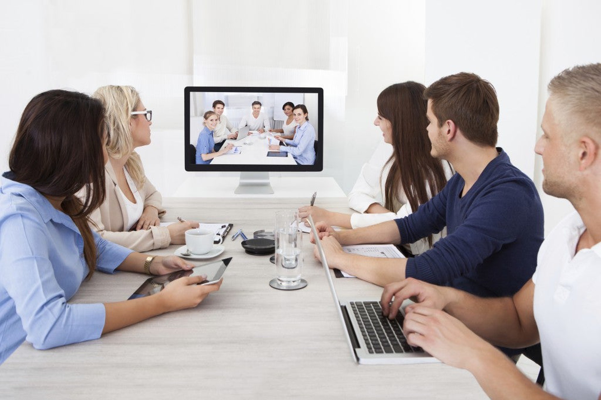 Five people in a meeting looking at five other people on a videoscreen